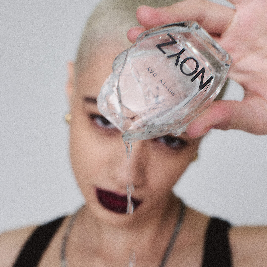 A model holds a broken bottle of NOYZ Sh**ty Day perfume showing the unisex fragrance