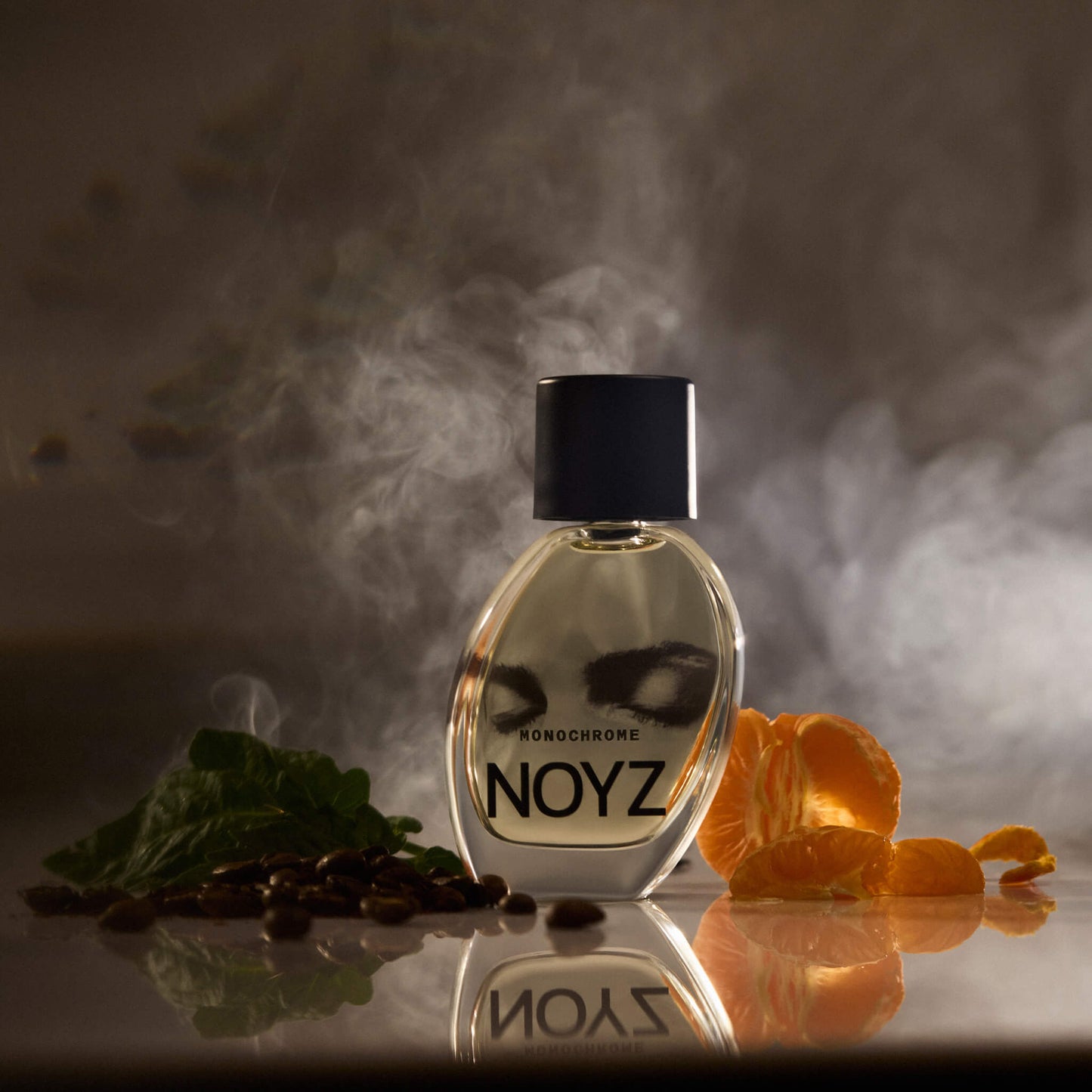 A bottle of Noyz Monochrome perfume in a moody environment surrounded citrus fruit, musk, patchouli and coffee beans