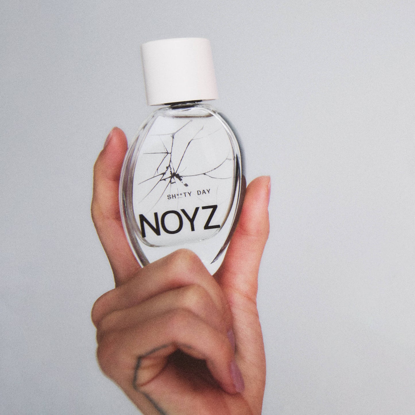 An upraised hand holds a 50 ml glass bottle of Noyz Sh**ty Day fragrance shows the top summer fragrances