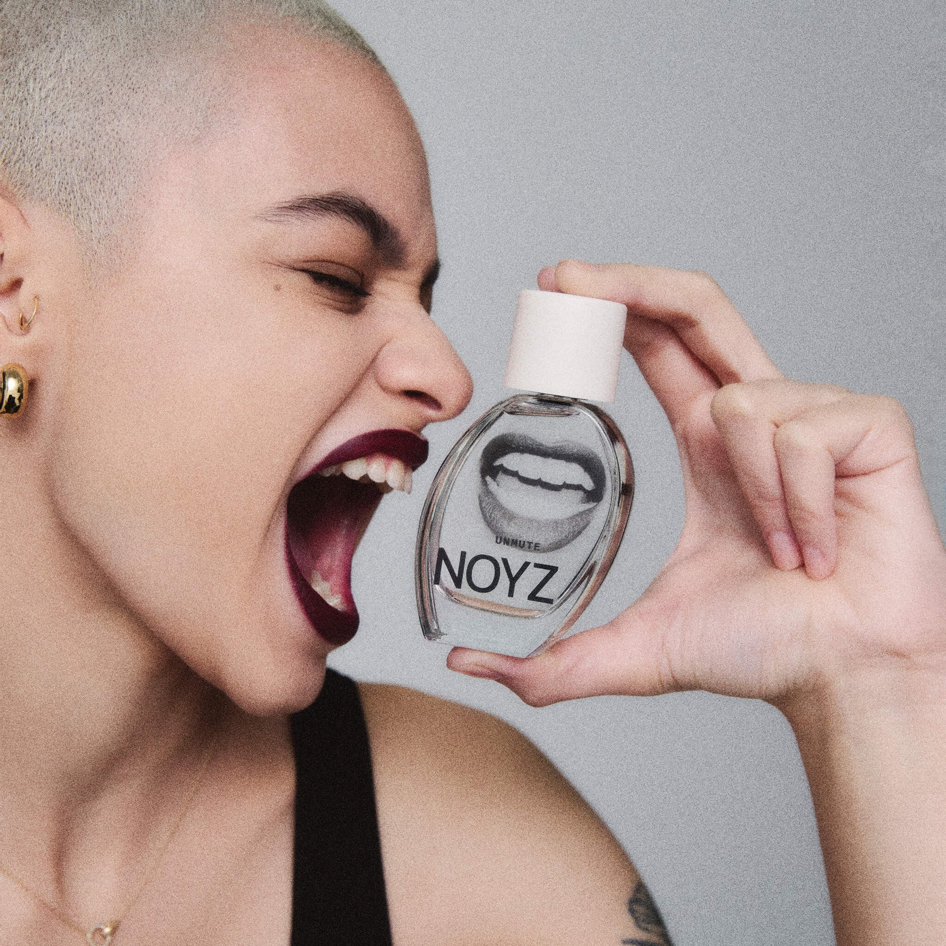 A model holds a bottle of NOYZ perfume Unmute. Explore citrus notes in this vanilla and amber scent