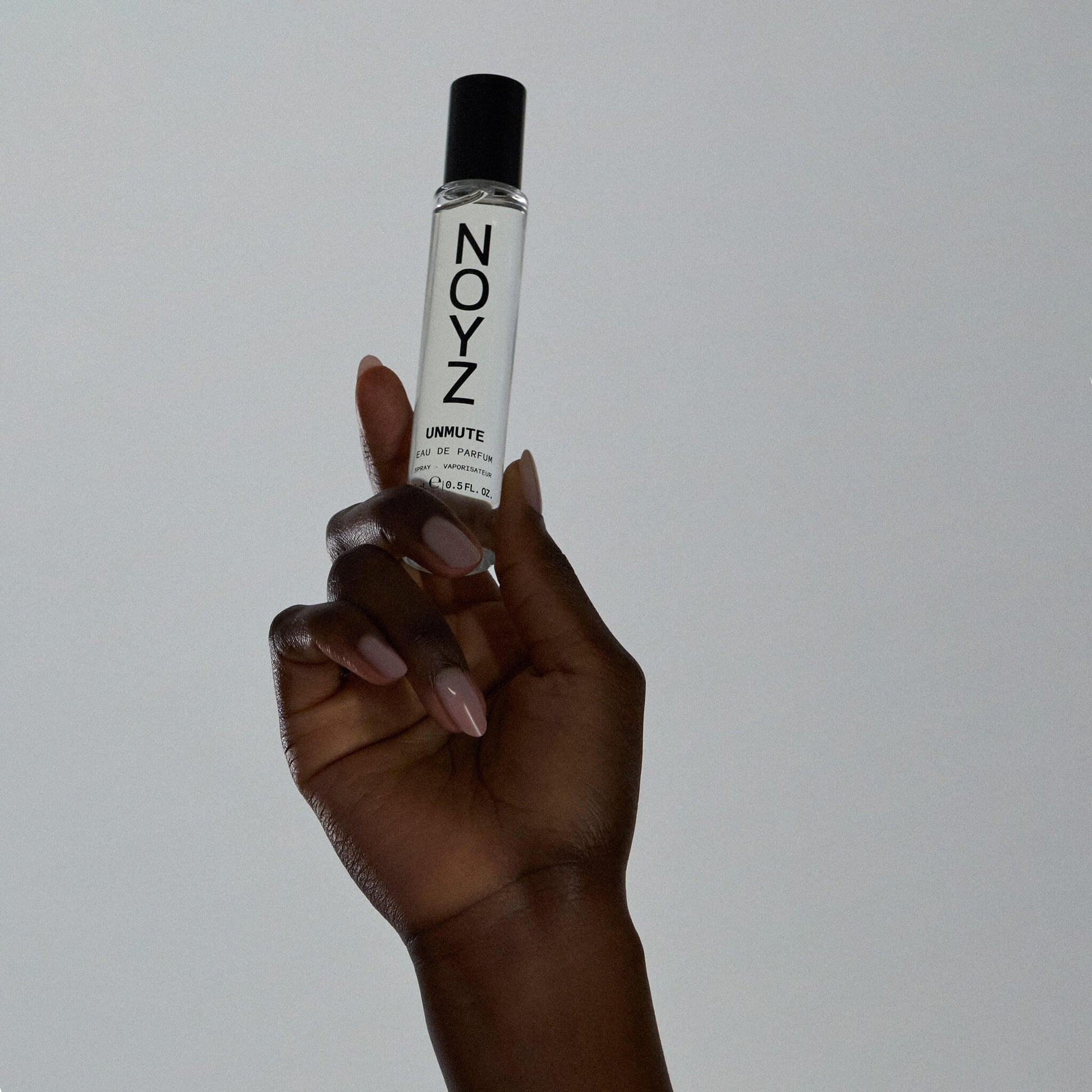 An upraised hand holds a small glass bottle of Noyz Unmute fragrance shows the best unisex fragrance