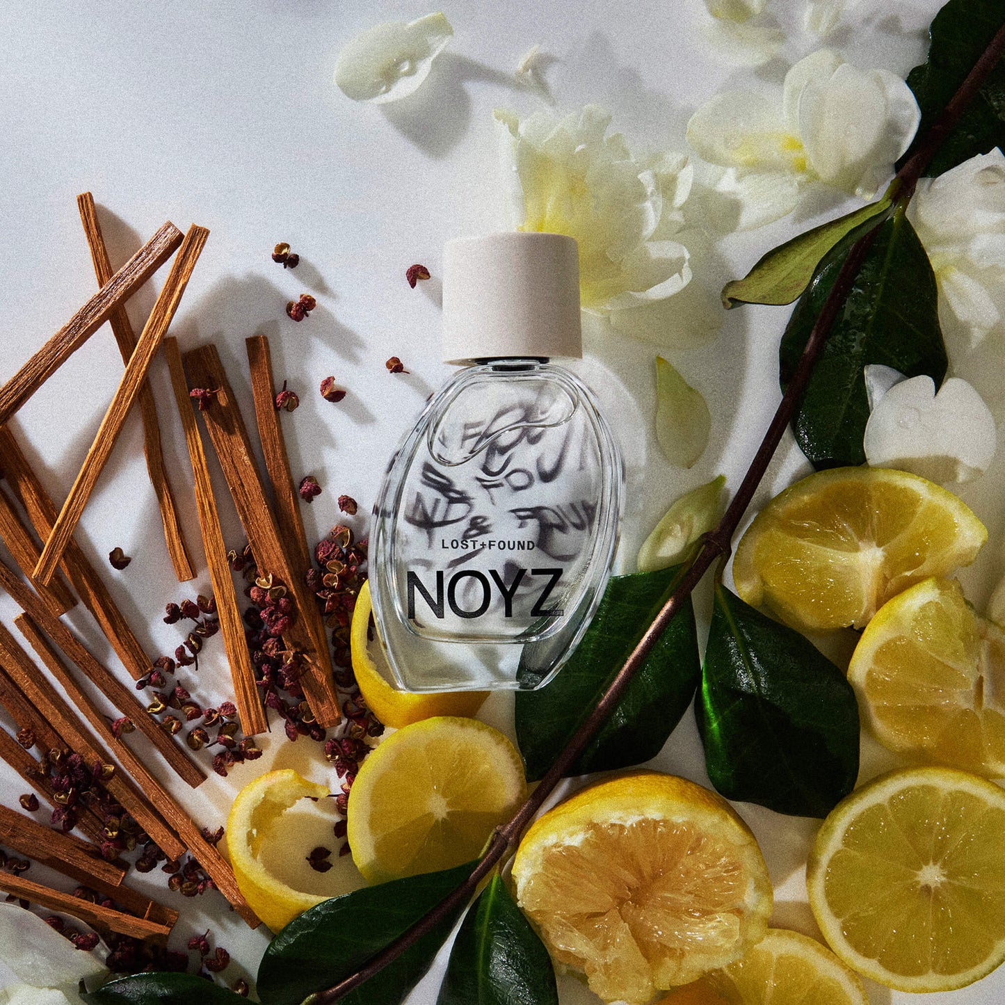 A bottle of Noyz perfume sits amidst cedarwood, italian lemon slices and jasmine flowers