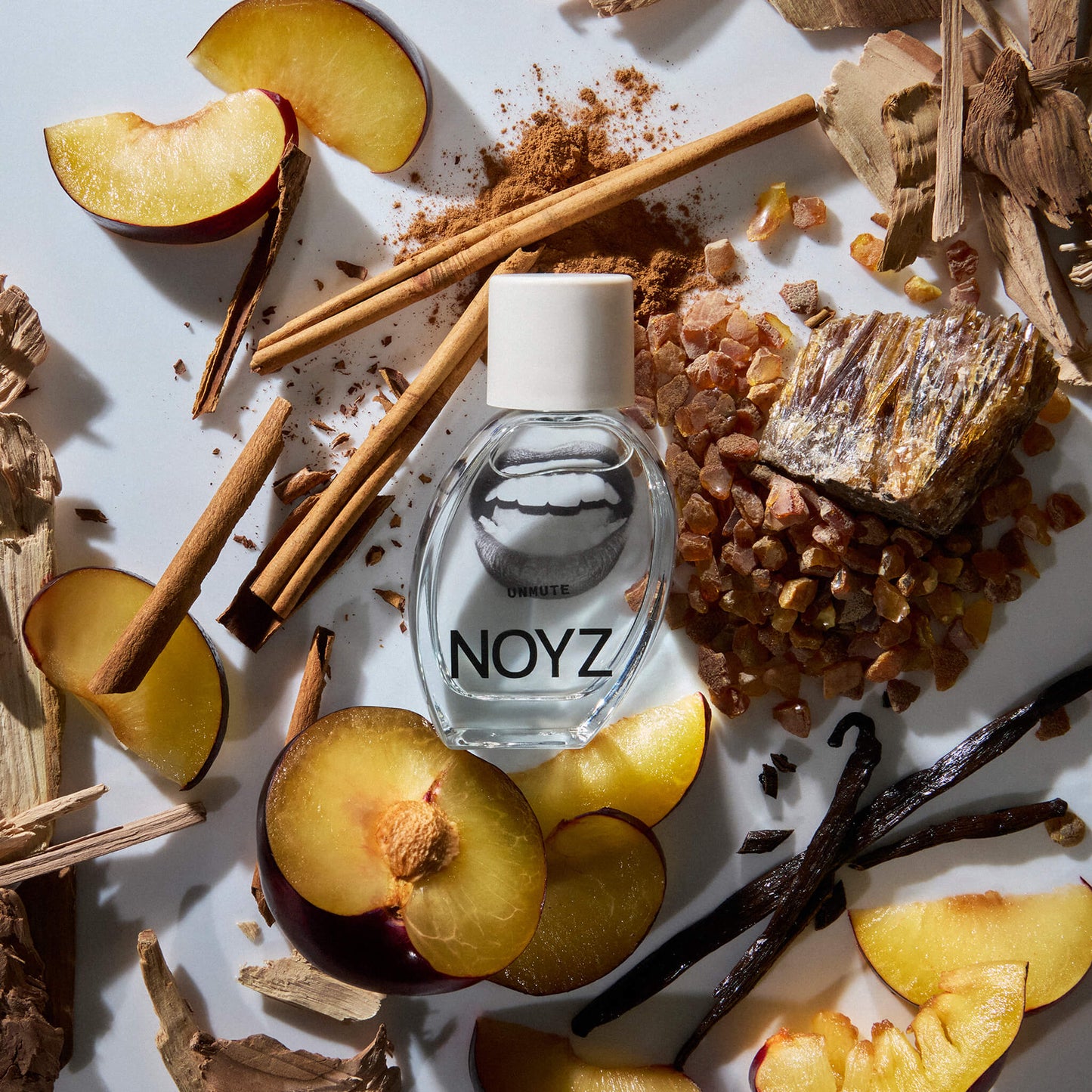 A bottle of NOYZ Unmute scent lays amidst vanilla sticks, Spanish ciste and black plums