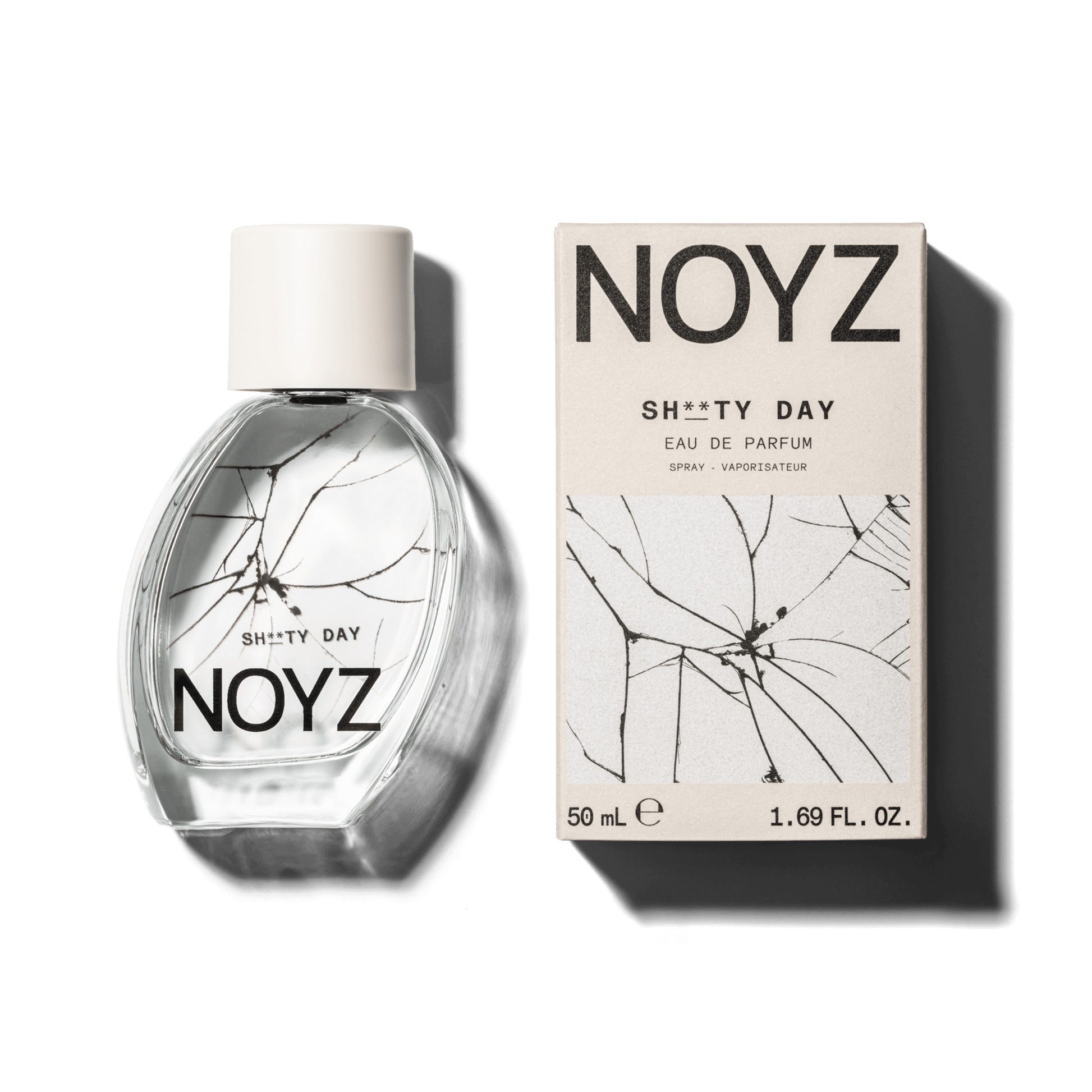 An asymmetrical glass bottle of top unisex fragrance Sh**ty Day by NOYZ next to a box of its sustainable packaging